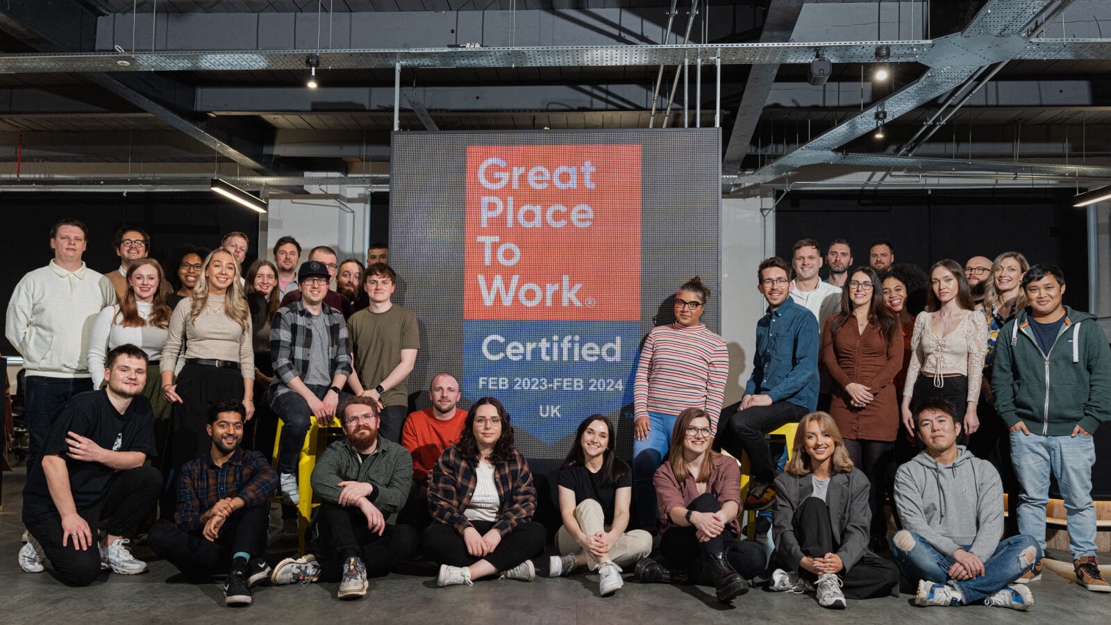 Engages team standing infront of the Great Place to Work Certification logo